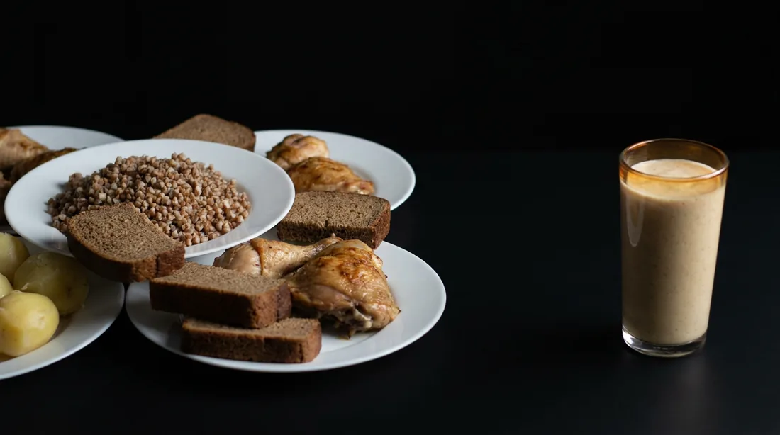 Тарелки с гречкой, курицей, картофелем и хлебом рядом со стаканом густого коктейля